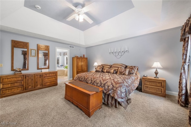 carpeted bedroom with a raised ceiling, ensuite bath, and ceiling fan