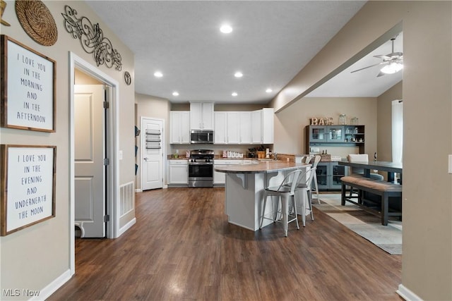 kitchen featuring a breakfast bar, stainless steel appliances, ceiling fan, dark wood-type flooring, and white cabinets