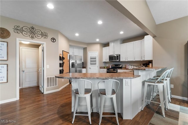 kitchen featuring white cabinets, appliances with stainless steel finishes, dark hardwood / wood-style floors, and a kitchen breakfast bar