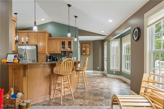 kitchen with stone counters, hanging light fixtures, kitchen peninsula, stainless steel fridge, and lofted ceiling