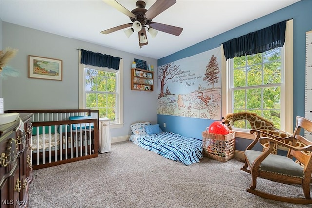 carpeted bedroom with a crib, multiple windows, and ceiling fan