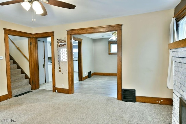 unfurnished living room featuring ceiling fan, light colored carpet, and a brick fireplace