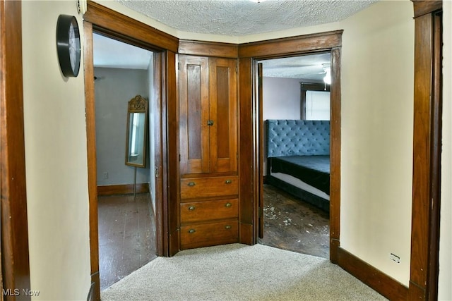 hall with a textured ceiling and dark carpet