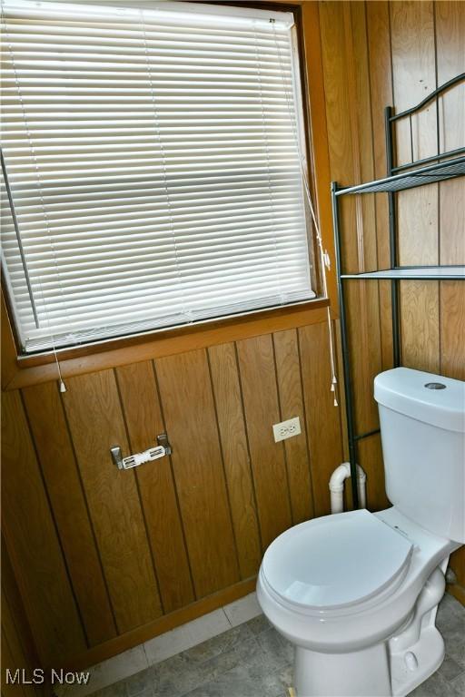 bathroom featuring tile patterned flooring, wood walls, and toilet