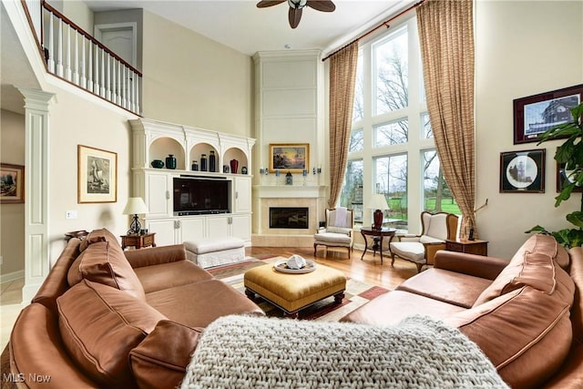 living room featuring a towering ceiling, decorative columns, ceiling fan, a fireplace, and hardwood / wood-style floors