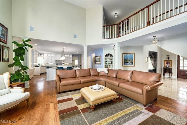 living room with ornate columns, a towering ceiling, and wood-type flooring