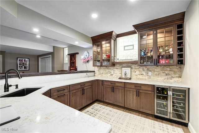 kitchen with tasteful backsplash, light stone counters, sink, light hardwood / wood-style floors, and wine cooler