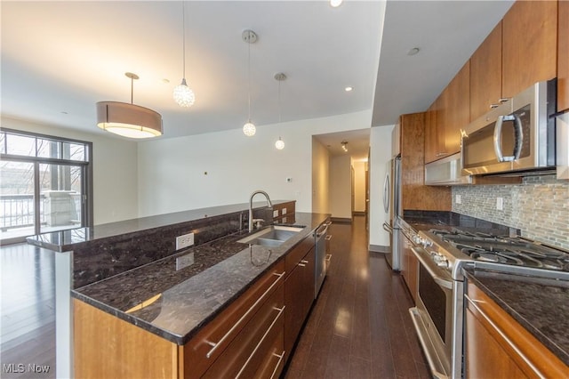 kitchen with stainless steel appliances, dark wood-type flooring, sink, pendant lighting, and a center island with sink