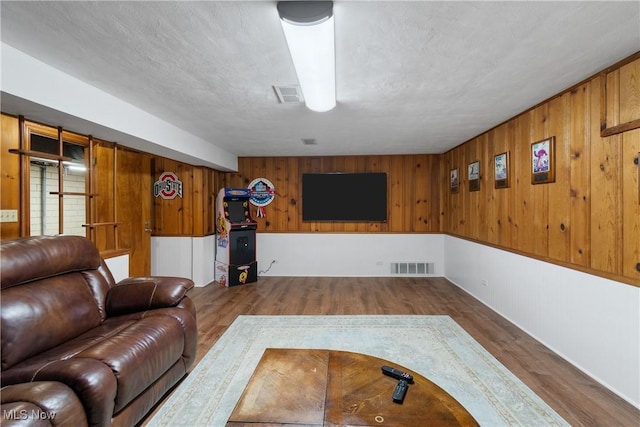 living room with wood walls, wood-type flooring, and a textured ceiling