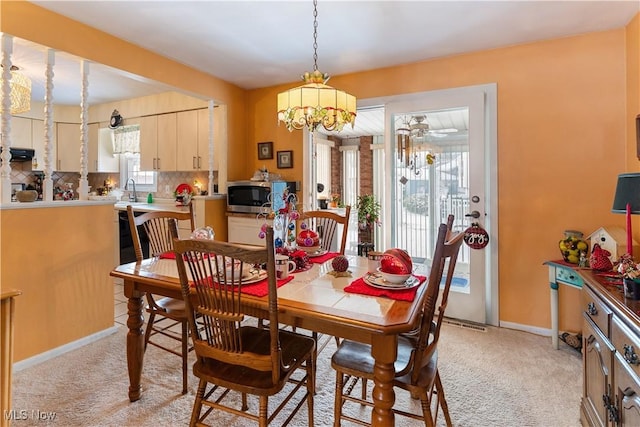 dining space with sink, light carpet, and a chandelier