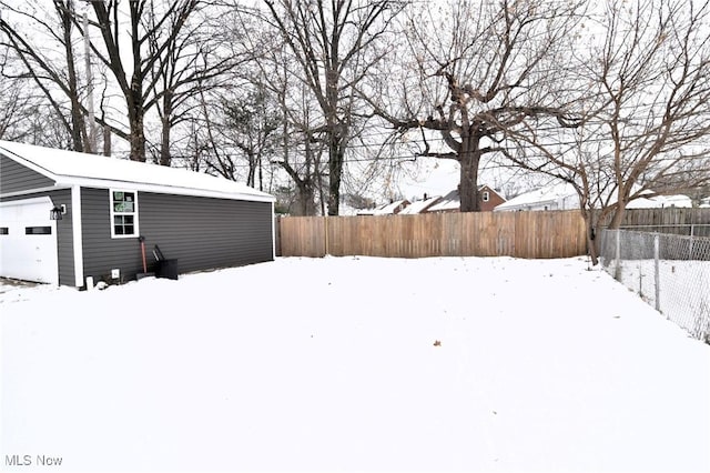 yard layered in snow featuring a garage and an outbuilding