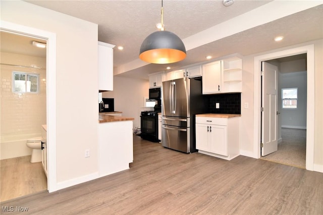 kitchen with white cabinetry, hanging light fixtures, light hardwood / wood-style flooring, wooden counters, and black appliances