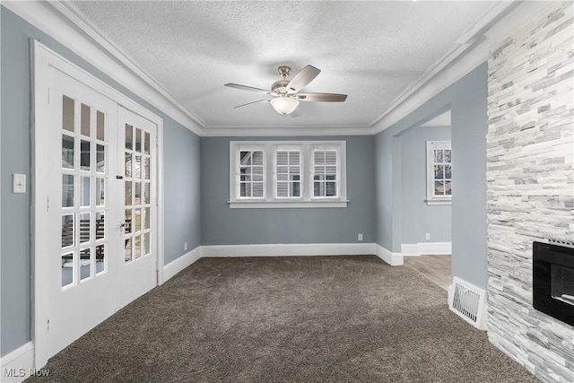 unfurnished room with a stone fireplace, crown molding, carpet, and a textured ceiling