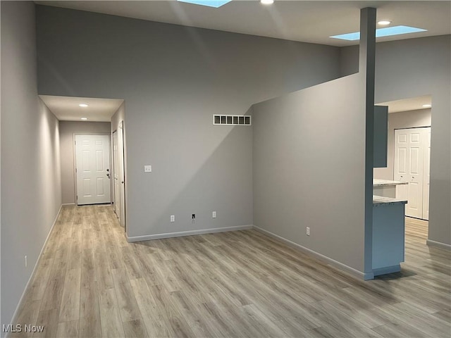 unfurnished living room with light hardwood / wood-style floors, a towering ceiling, and a skylight