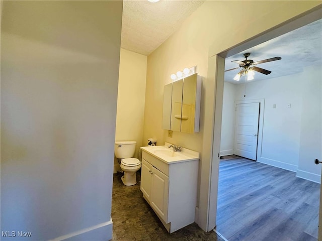 bathroom with ceiling fan, wood-type flooring, a textured ceiling, toilet, and vanity