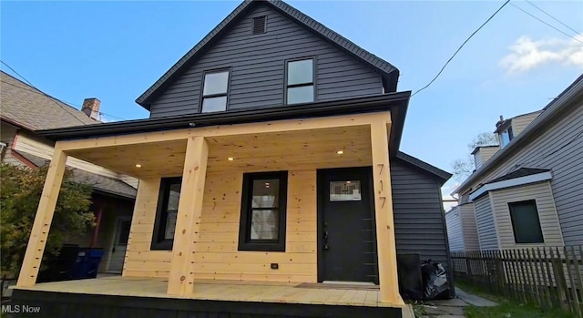 rear view of property with covered porch and fence