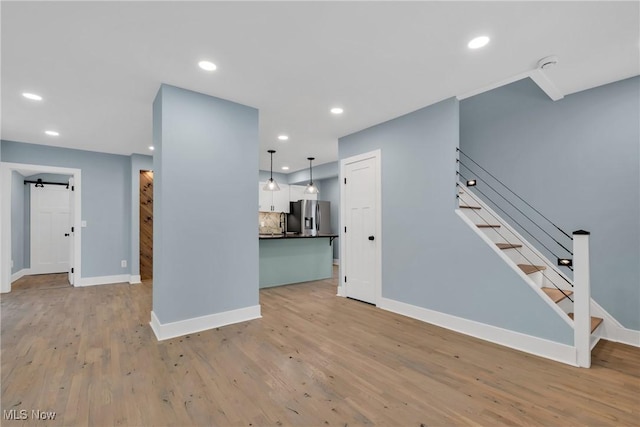 unfurnished living room with a barn door, baseboards, light wood-style flooring, stairs, and recessed lighting