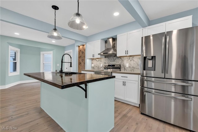 kitchen with light wood finished floors, tasteful backsplash, wall chimney exhaust hood, appliances with stainless steel finishes, and a sink