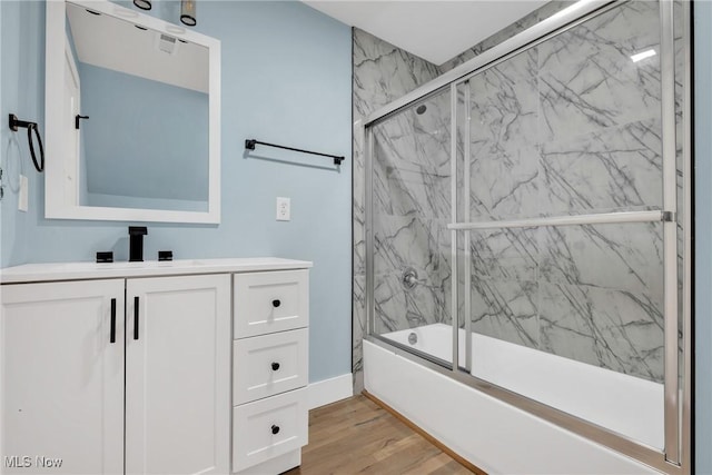 full bath featuring wood finished floors, vanity, baseboards, and bath / shower combo with glass door