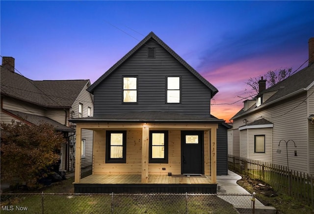 back of house at dusk featuring a porch and a fenced front yard