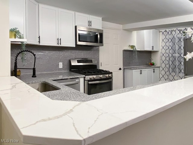 kitchen featuring sink, backsplash, kitchen peninsula, white cabinets, and appliances with stainless steel finishes