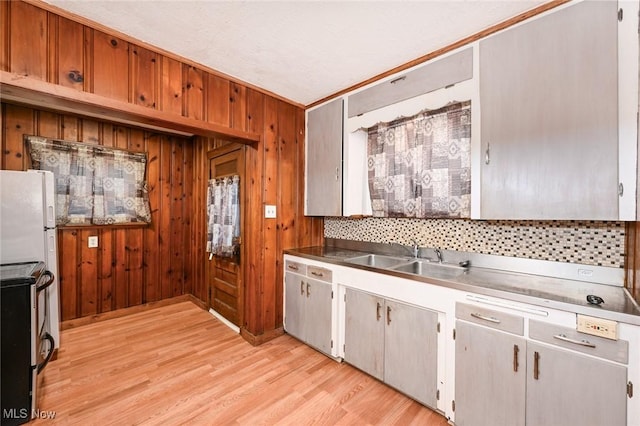 kitchen featuring crown molding, sink, wooden walls, and light wood-type flooring