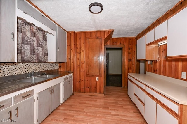 kitchen with sink, crown molding, light wood-type flooring, a textured ceiling, and white cabinetry