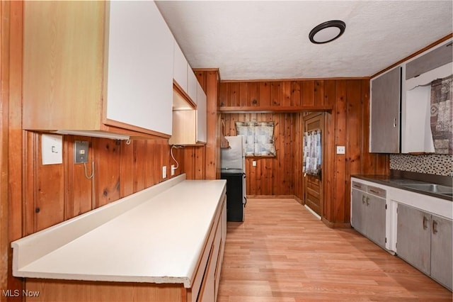 kitchen with light wood-type flooring, refrigerator, a textured ceiling, wooden walls, and sink