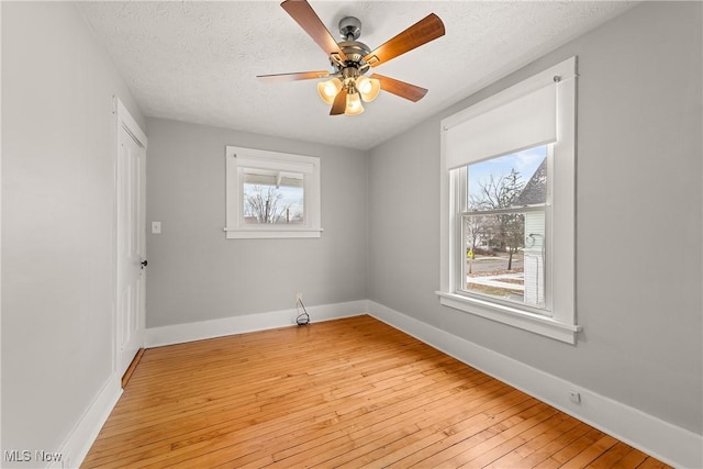 spare room with a textured ceiling, light wood-type flooring, a wealth of natural light, and ceiling fan