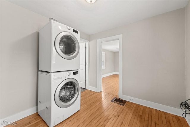 washroom with light hardwood / wood-style floors and stacked washer / drying machine