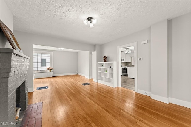 unfurnished living room with a fireplace, ceiling fan, hardwood / wood-style floors, and a textured ceiling