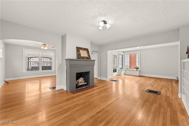 unfurnished living room featuring a textured ceiling, light hardwood / wood-style floors, a brick fireplace, and ceiling fan