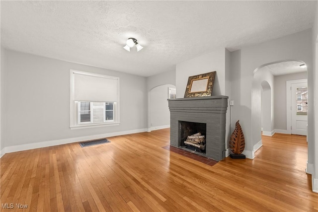 unfurnished living room with light hardwood / wood-style flooring, a textured ceiling, and a brick fireplace