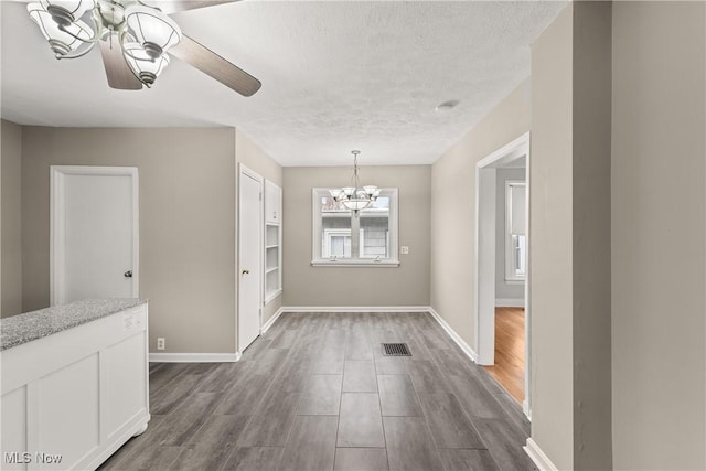 unfurnished dining area with wood-type flooring, ceiling fan with notable chandelier, and a textured ceiling