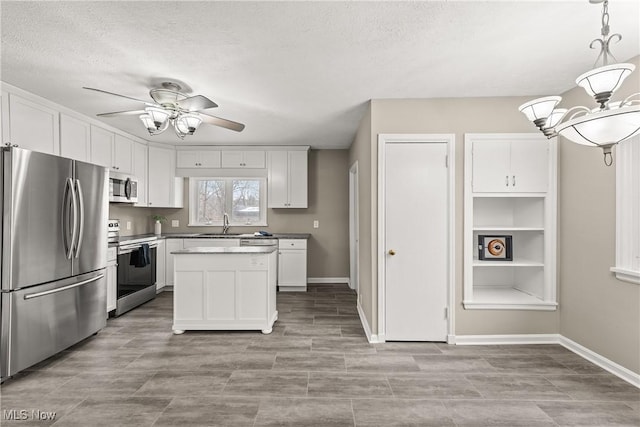 kitchen with white cabinets, hanging light fixtures, a textured ceiling, appliances with stainless steel finishes, and a kitchen island