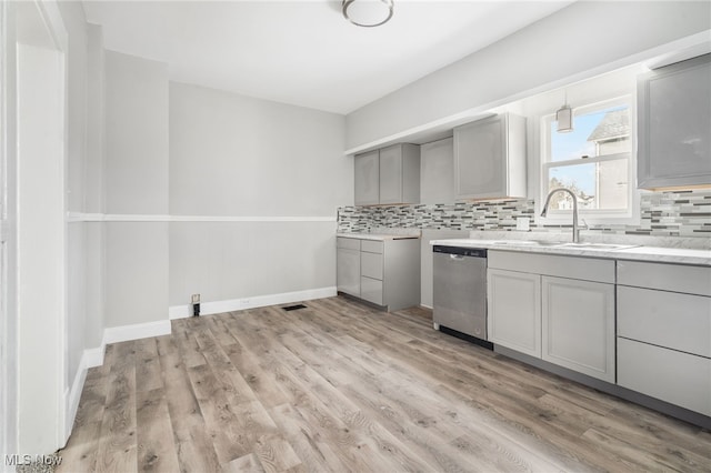 kitchen with tasteful backsplash, stainless steel dishwasher, gray cabinetry, sink, and light hardwood / wood-style flooring