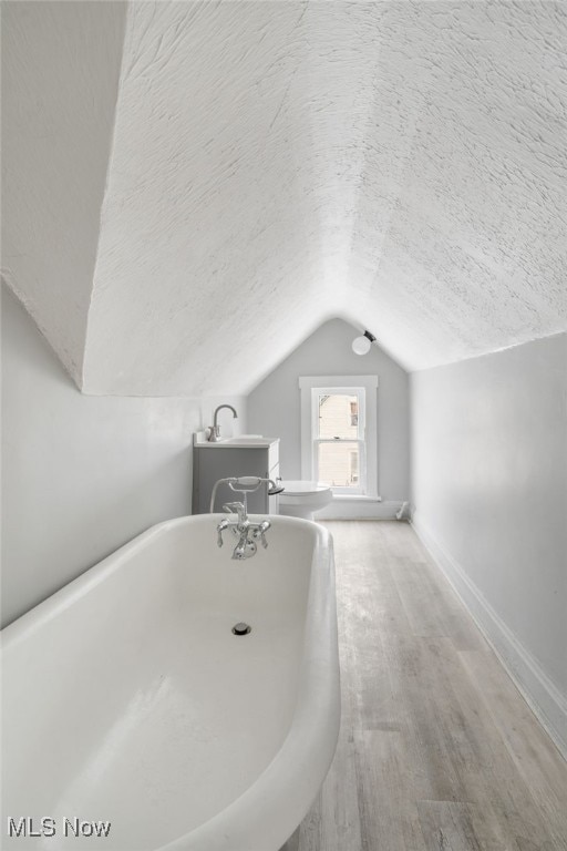 bathroom with a textured ceiling, hardwood / wood-style floors, lofted ceiling, toilet, and a bathing tub