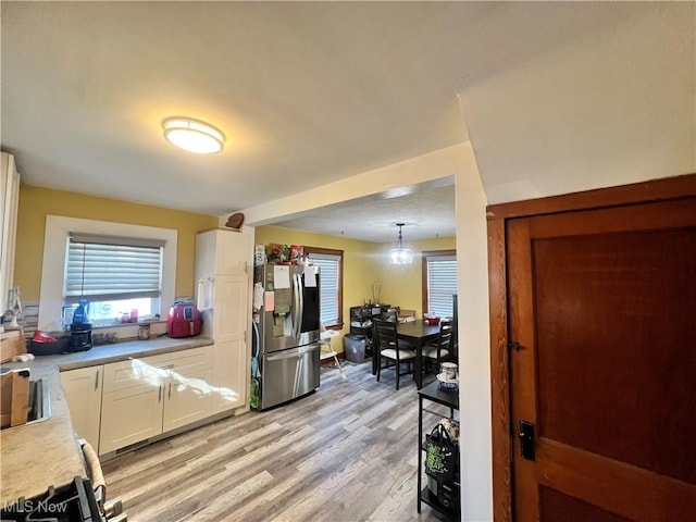 kitchen featuring sink, decorative light fixtures, light hardwood / wood-style flooring, stainless steel fridge with ice dispenser, and white cabinetry