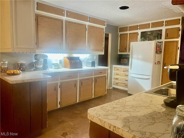 kitchen featuring a textured ceiling, white refrigerator, concrete floors, and sink