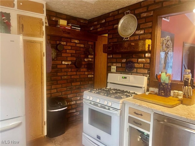 kitchen with a textured ceiling, white appliances, and brick wall