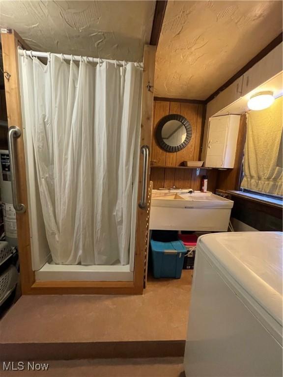 bathroom with washer / clothes dryer, wooden walls, sink, and a shower with shower curtain