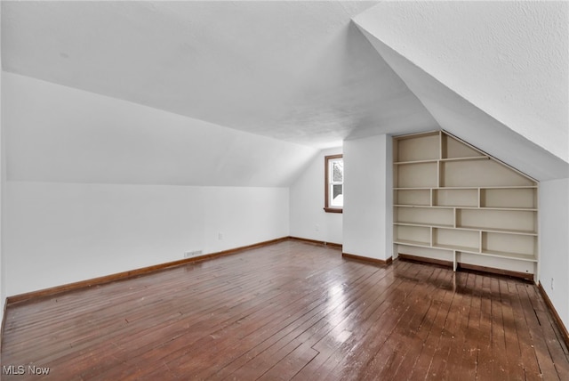 additional living space with a textured ceiling, built in shelves, vaulted ceiling, and hardwood / wood-style flooring