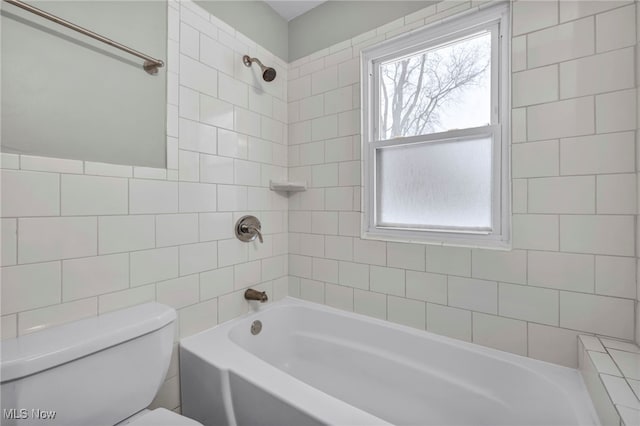 bathroom featuring tiled shower / bath combo, toilet, and tile walls