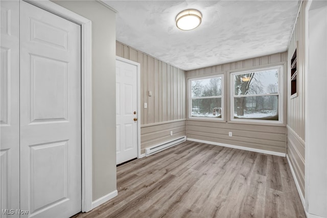 unfurnished room featuring wood walls, light wood-type flooring, and a baseboard heating unit