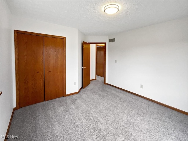 unfurnished bedroom featuring a textured ceiling, light colored carpet, and a closet