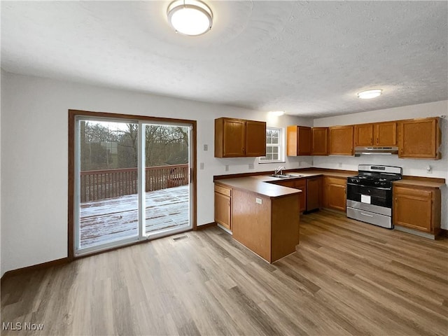 kitchen with a textured ceiling, sink, light hardwood / wood-style floors, and stainless steel range with gas stovetop