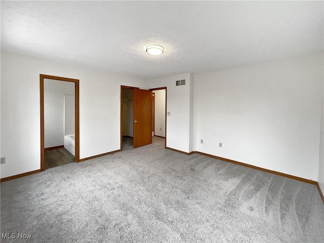 unfurnished bedroom with ensuite bath, carpet, and a textured ceiling