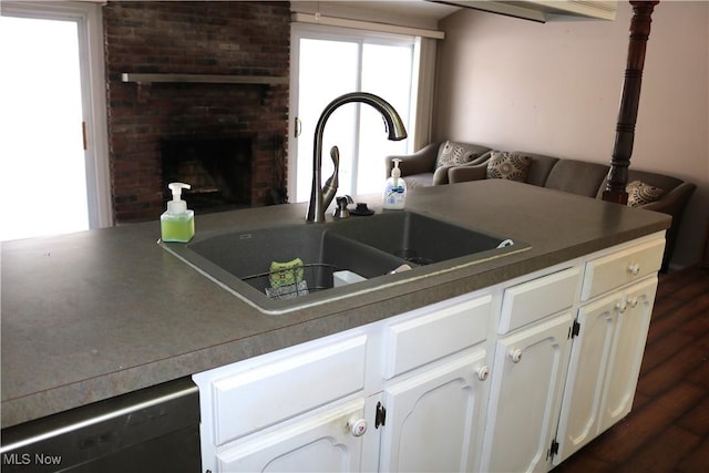 kitchen with a brick fireplace, stainless steel dishwasher, dark wood-type flooring, sink, and white cabinetry