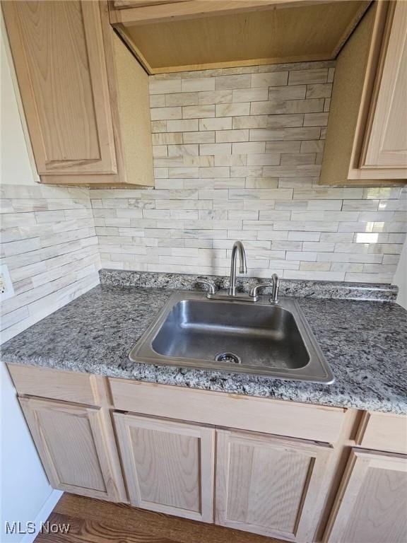 kitchen with sink, backsplash, dark stone counters, wood-type flooring, and light brown cabinetry