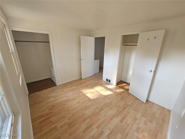 unfurnished bedroom with multiple closets and light hardwood / wood-style flooring